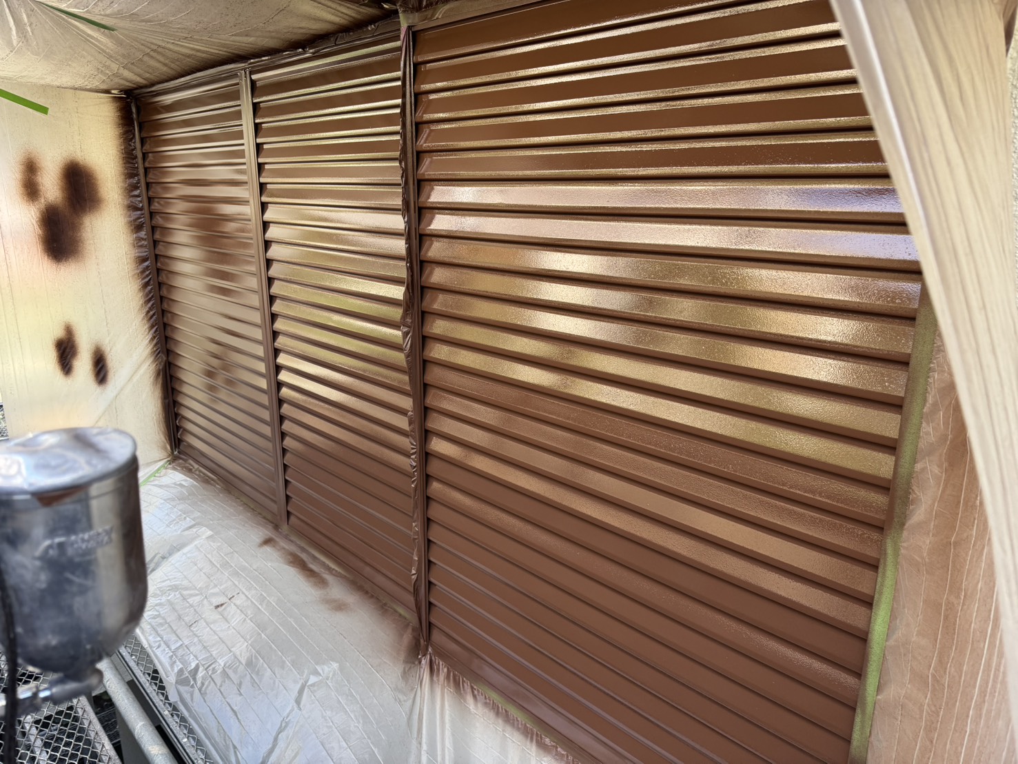 町田市K様邸の雨戸・戸袋吹き付け塗装作業。スプレーガンによる1回目塗布で塗膜を形成し、防錆性と美観を向上させる外壁付帯部塗装の施工写真。